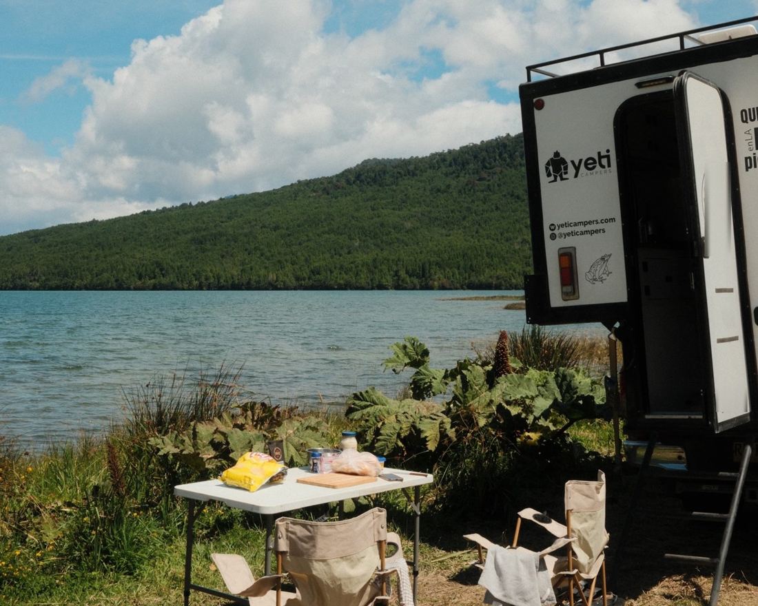 A folding table and chairs set up next to a Yeti camper on a lakeshore